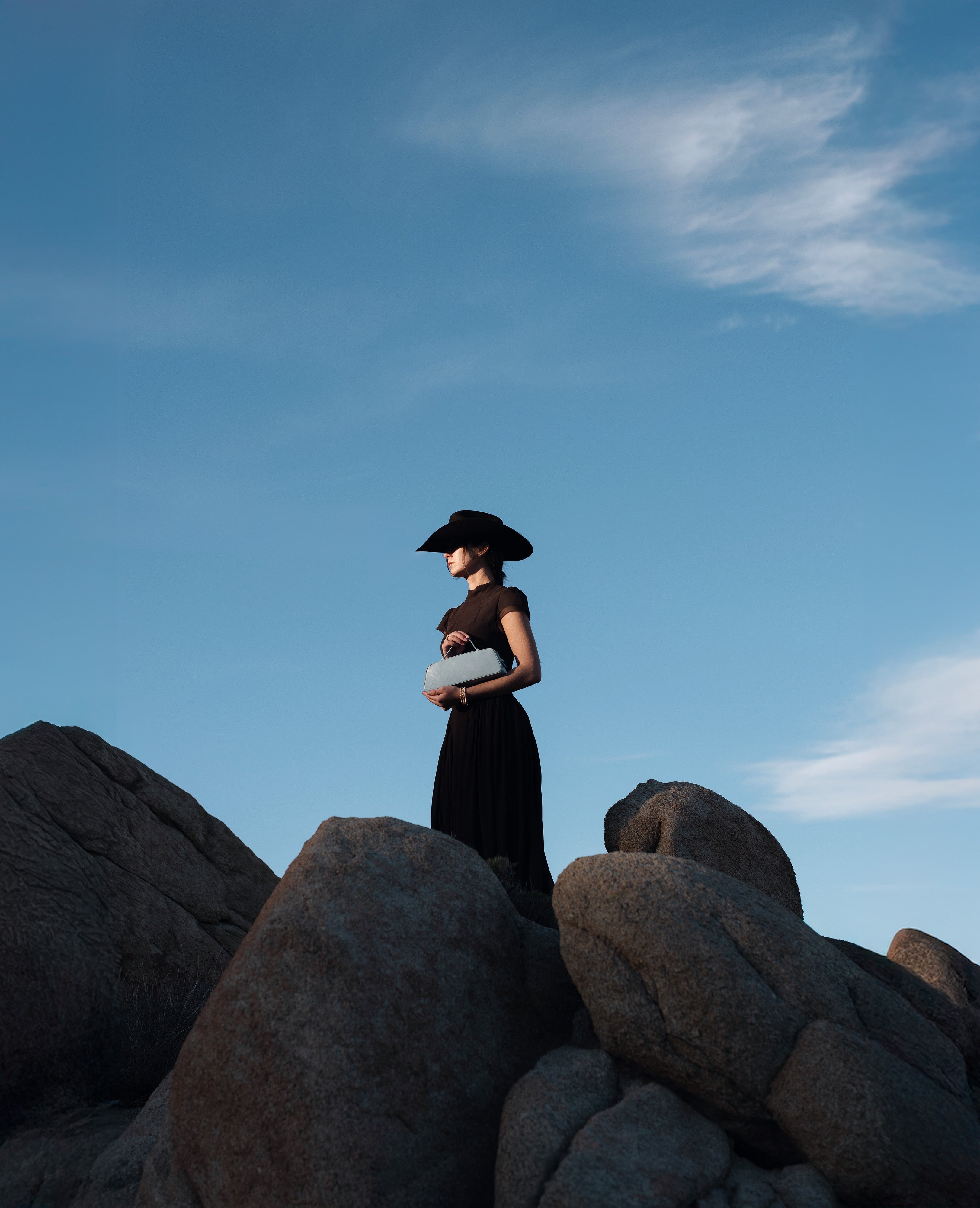 Person in a black outfit standing on large rocks with a blue sky background