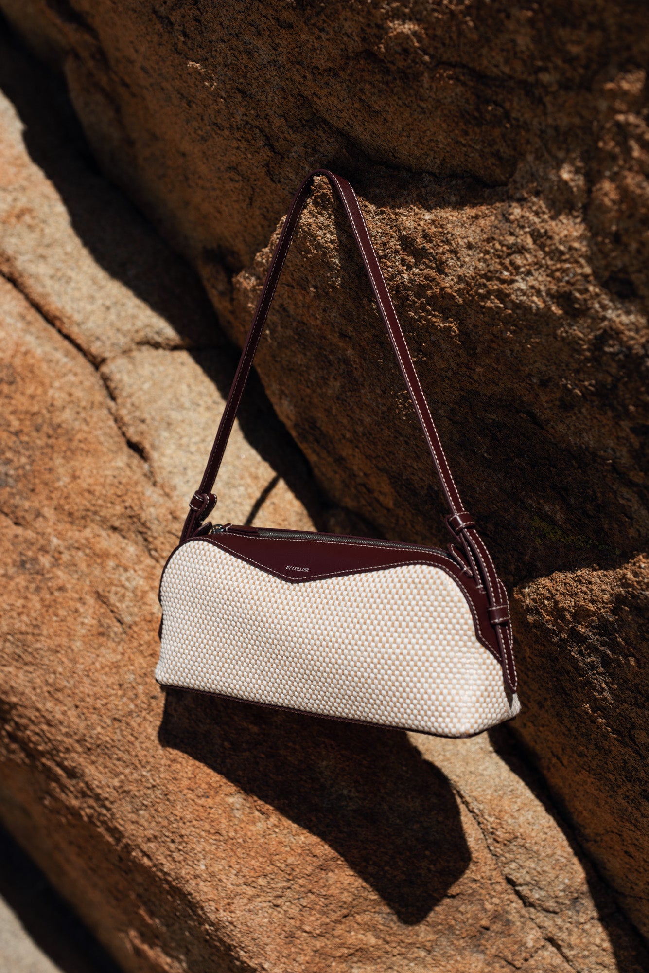 White handbag with brown strap on a rocky surface