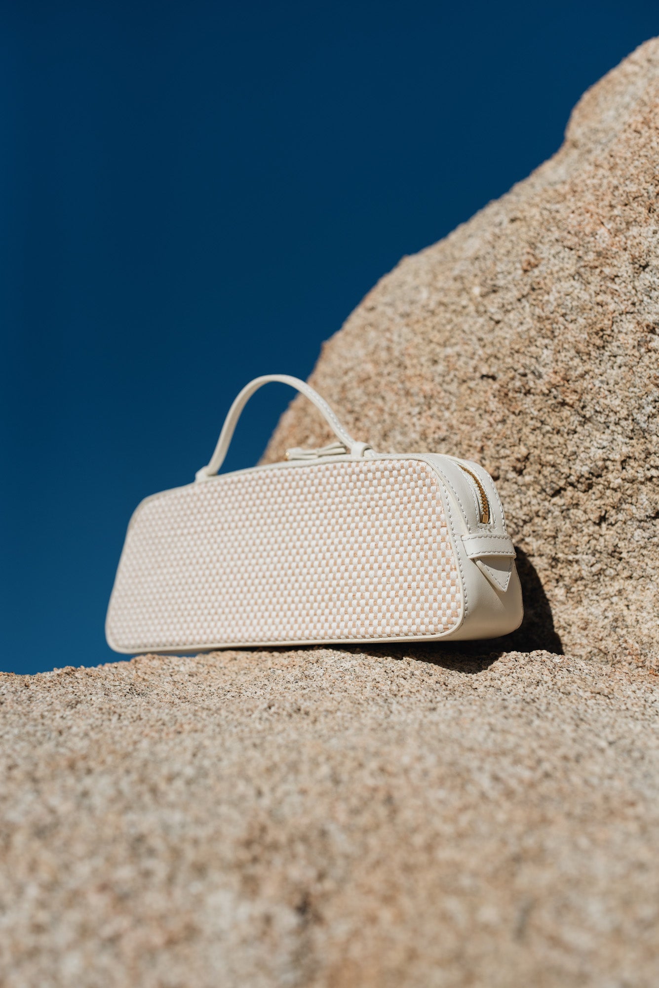Beige woven handbag on a sandy surface with a clear blue sky