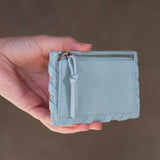 Light blue wallet held in a hand against a neutral background