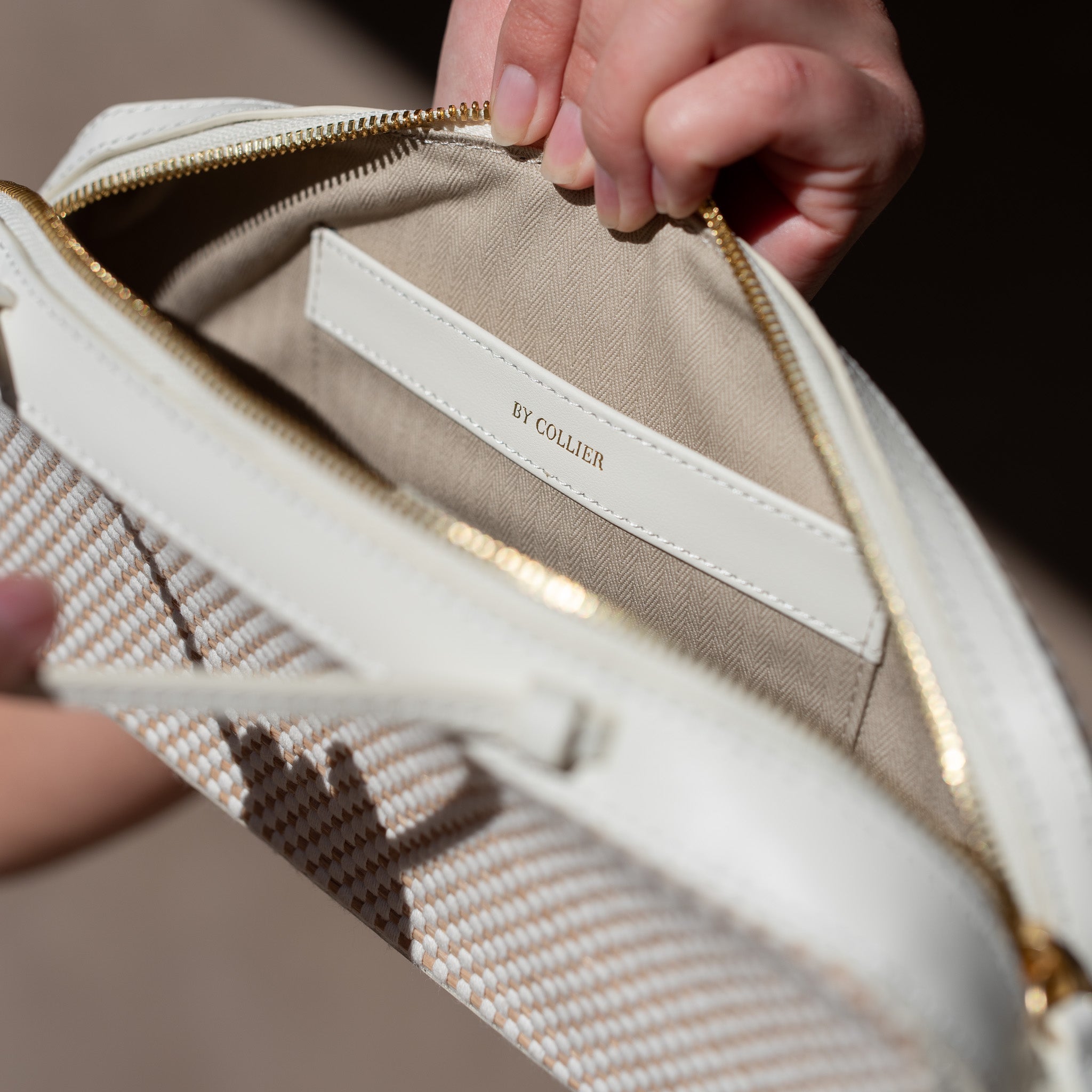 Close-up of a beige handbag with a brand label, held by a person.
