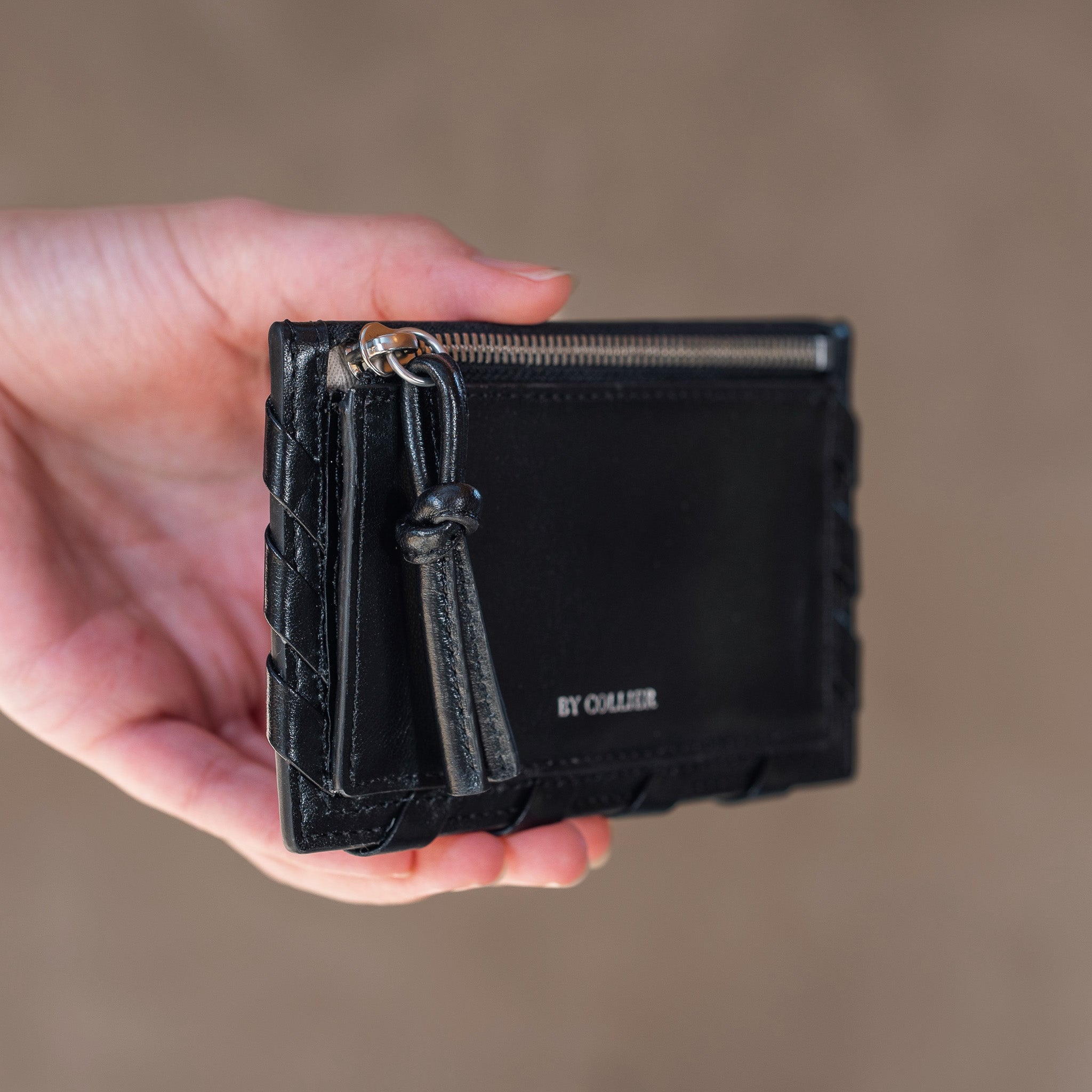 Black wallet held in a hand with a blurred background