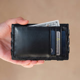 Hand holding a black leather wallet with money and cards on a beige background