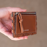 Brown leather wallet held in a hand against a blurred background