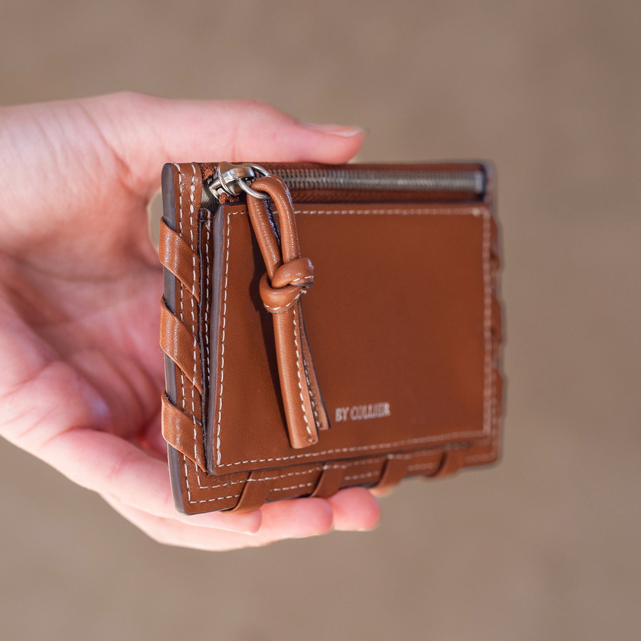 Brown leather wallet held in a hand against a blurred background