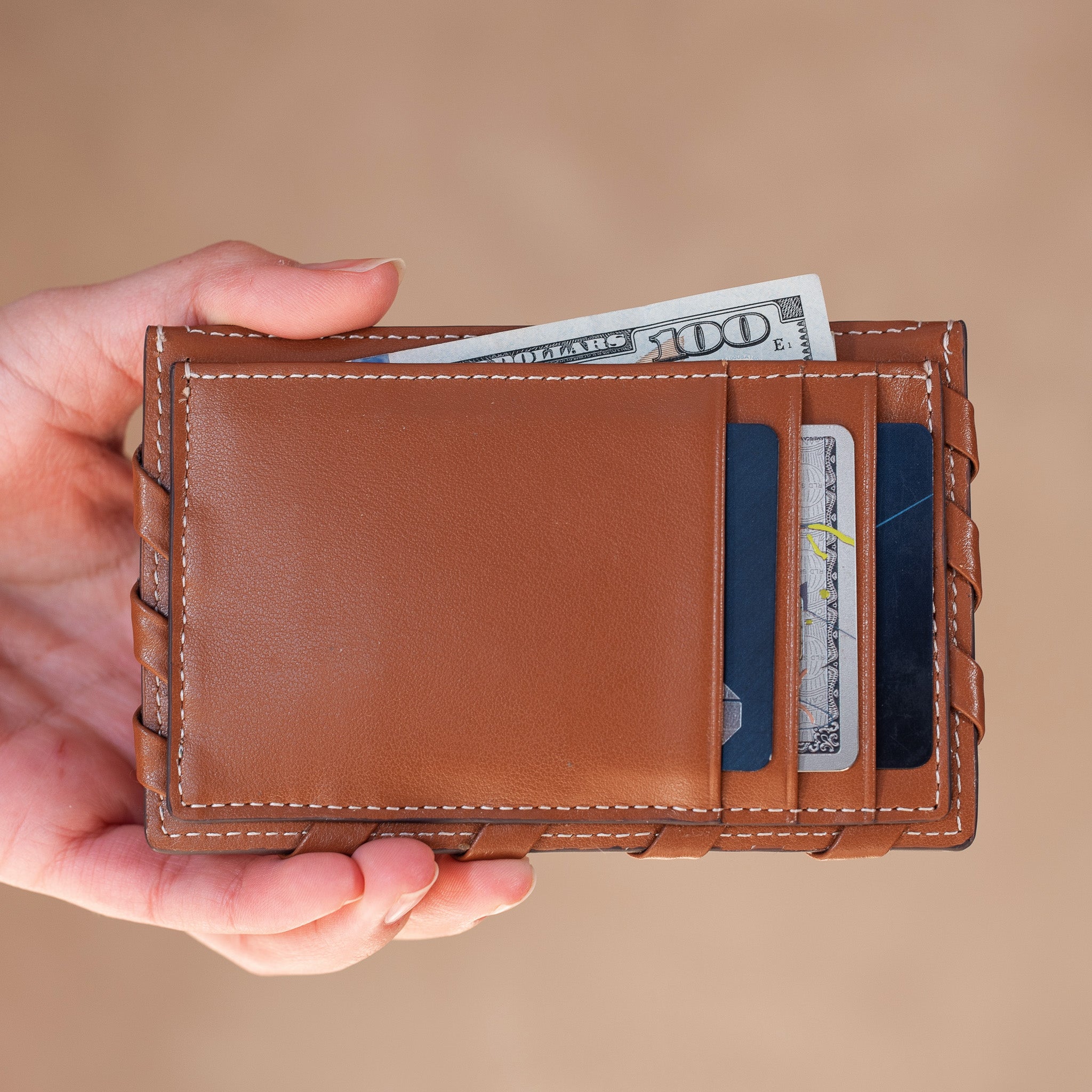 Brown leather wallet held by a hand with money and cards on a beige background