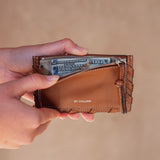 Brown leather wallet with money held open by a hand on a beige background