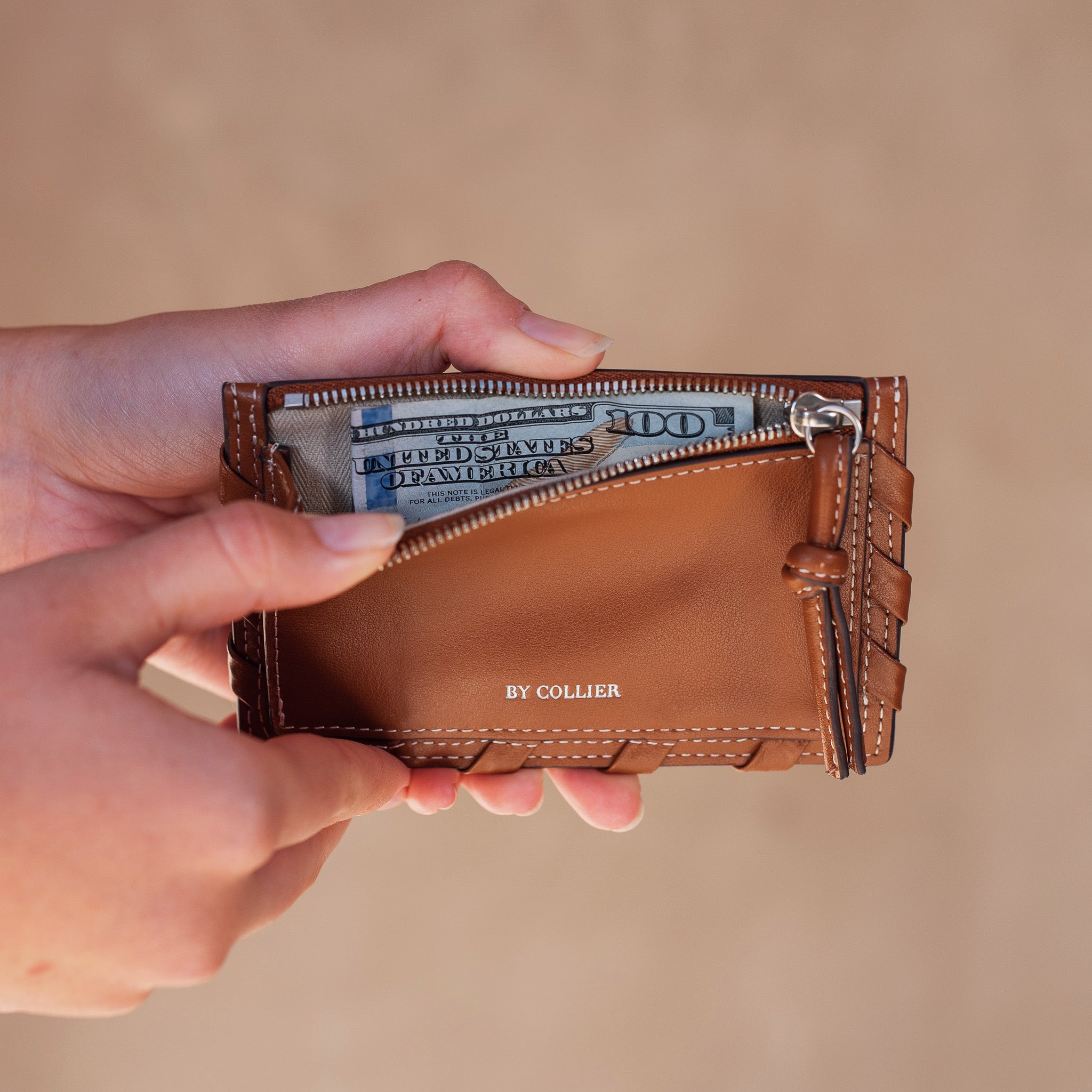 Brown leather wallet with money held open by a hand on a beige background