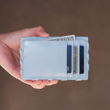 Light blue wallet held by a hand with money and cards on a brown background