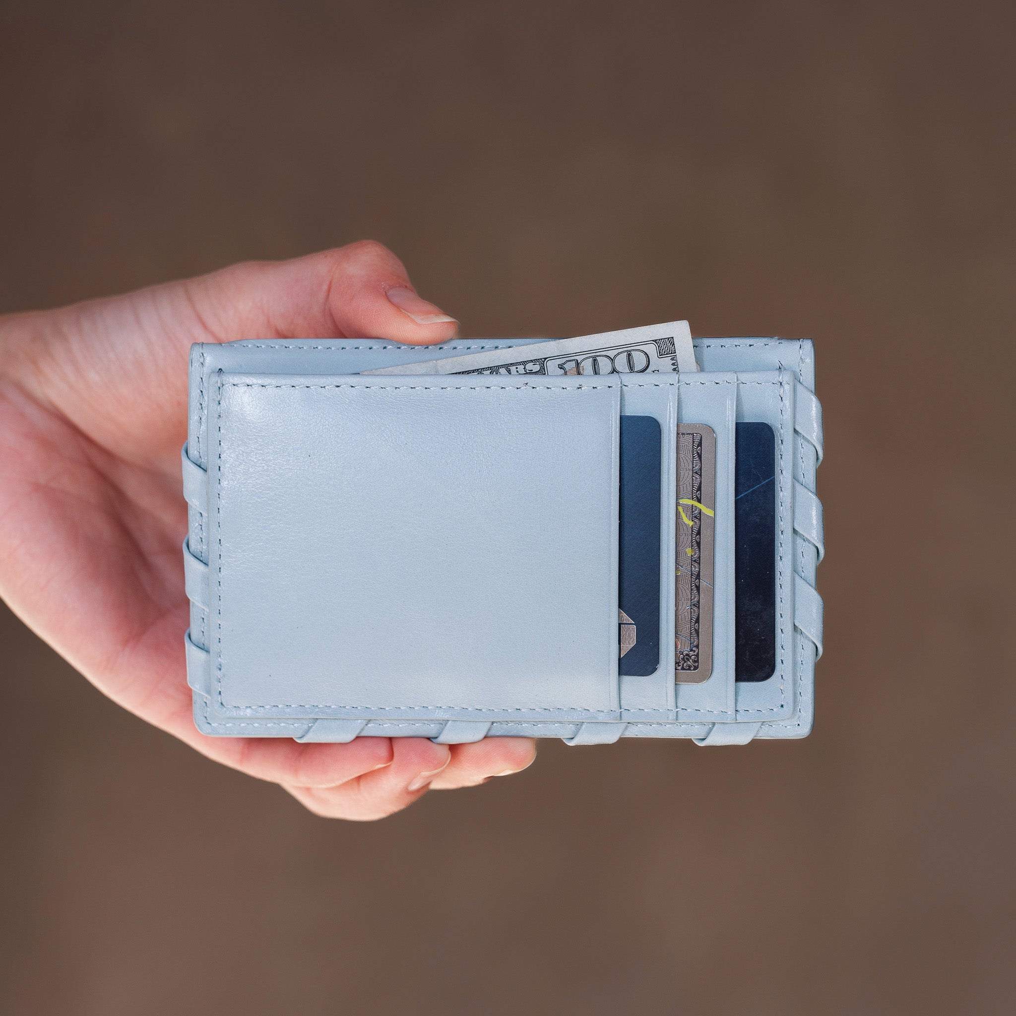 Light blue wallet held by a hand with money and cards on a brown background