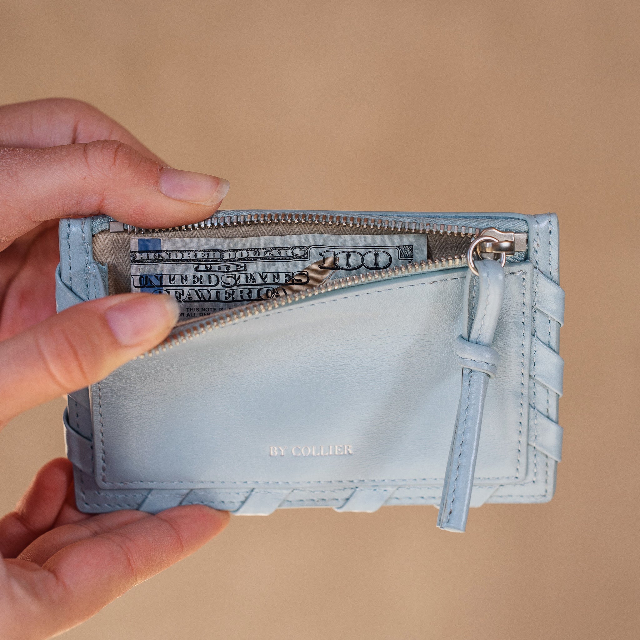 Light blue wallet with money held open by a hand against a beige background